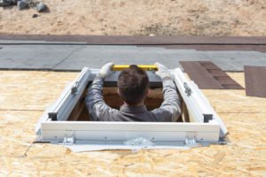 Worker on a asphalt shingle roof installing new plastic (mansard) or skylight window