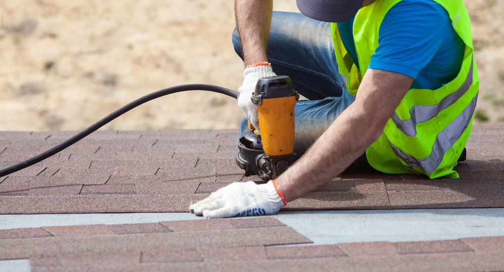 Roofer builder worker with nail gun installing Asphalt Shingles