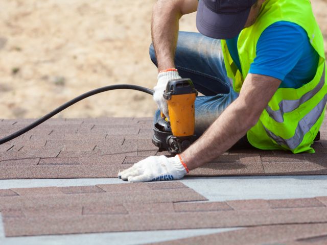 Roofer builder worker with nail gun installing Asphalt Shingles